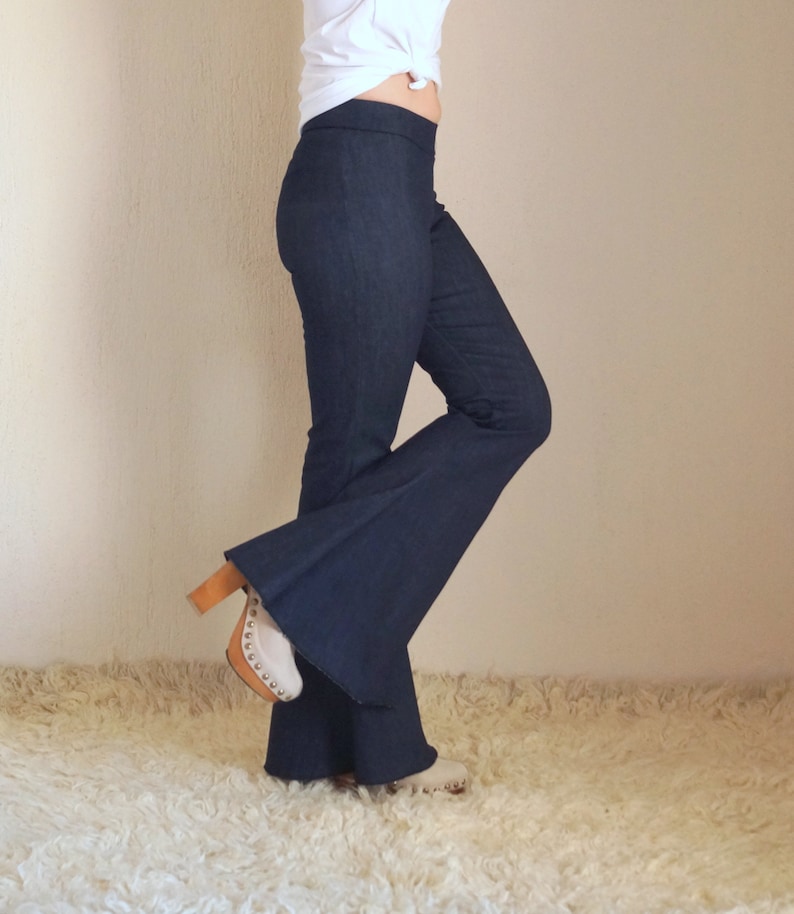 May include: Dark blue flared pants with a high waist. The pants are paired with white clogs with a wooden heel. The outfit is set against a neutral background and a white rug.