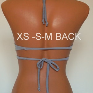 May include: Back view of a gray halter top bikini with adjustable straps. The top is tied at the back with a bow. The size label reads "XS-S-M BACK".