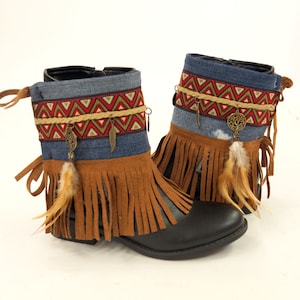 May include: A pair of brown suede ankle boots with fringe detailing. The boots have a denim upper with a patterned trim and metal accents.