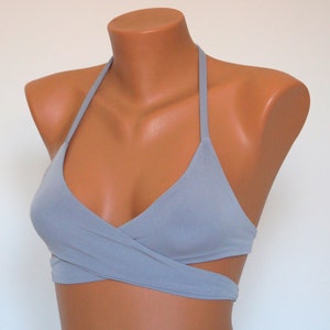May include: A light gray halter top with a criss-cross design in the front. The top has a scoop neckline and a wide strap.