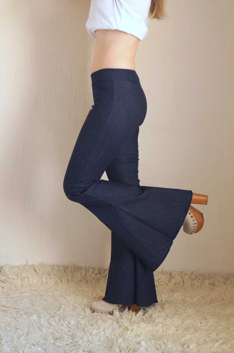 May include: Dark blue flared pants with a high waist. The pants are paired with wooden-heeled clogs. The pants are made of a denim-like material. The pants have a wide leg opening.