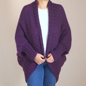 May include: A deep purple, open-front cardigan sweater with a shawl collar and ribbed cuffs. The sweater is made of a thick knit material and has a relaxed fit. The sleeves are long and the body is mid-length.