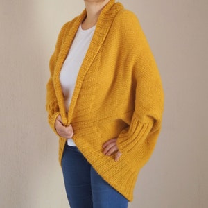Puede incluir: Un c&aacute;rdigan de punto amarillo mostaza con cuello ancho y mangas largas. El c&aacute;rdigan est&aacute; abierto por delante y tiene un corte holgado.