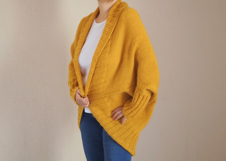 Puede incluir: Un c&aacute;rdigan de punto amarillo mostaza con cuello ancho y mangas largas. El c&aacute;rdigan est&aacute; abierto por delante y tiene un corte holgado.