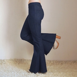 May include: Dark blue denim flare pants. The pants have a high waist and a wide, flared leg. The model is wearing the pants with a pair of wooden-heeled shoes with a light-colored toe.