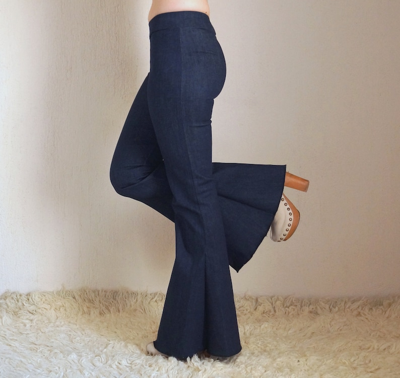 May include: Dark blue denim flare pants. The pants have a high waist and a wide, flared leg. The model is wearing the pants with a pair of wooden-heeled shoes with a light-colored toe.