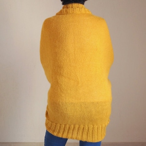Puede incluir: Un su&eacute;ter largo de punto amarillo con cuello alto.