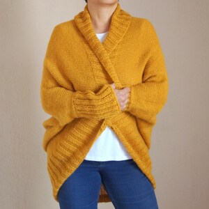 Puede incluir: Un c&aacute;rdigan de punto amarillo mostaza con cuello ancho y mangas largas.