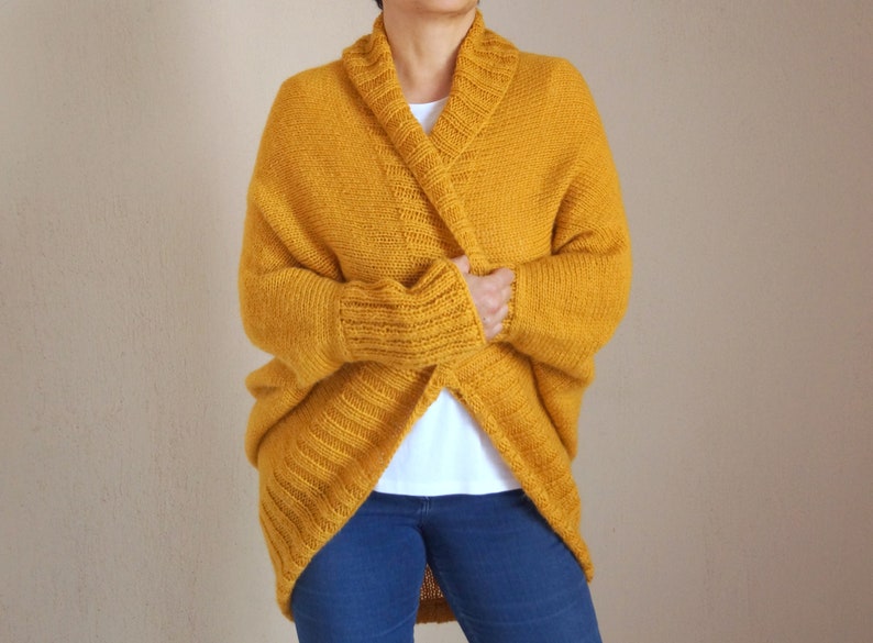 Puede incluir: Un c&aacute;rdigan de punto amarillo mostaza con cuello ancho y mangas largas.