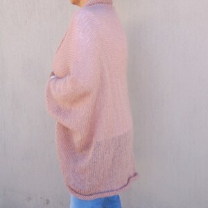 May include: A soft, pink knitted cardigan with a loose, oversized fit. The cardigan has long sleeves and a slightly cropped length.
