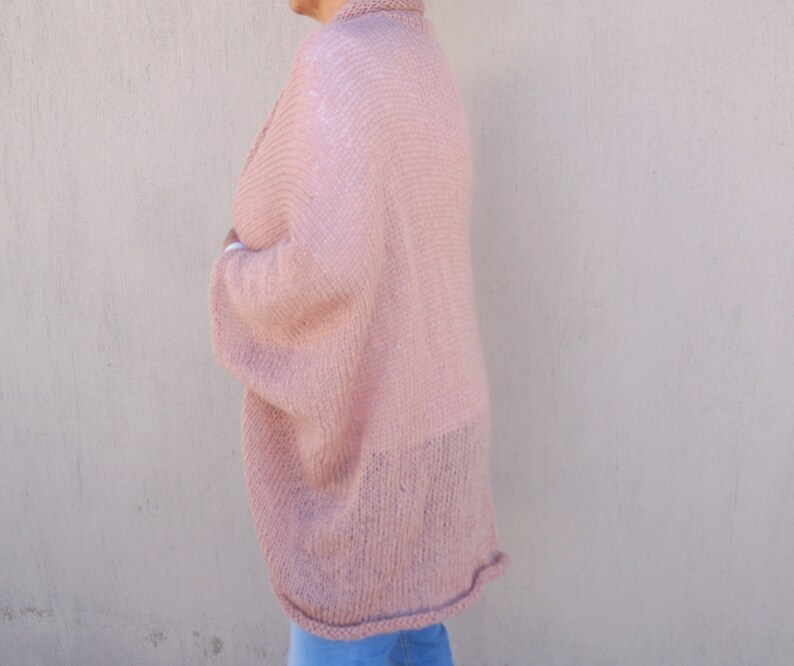 May include: A soft, pink knitted cardigan with a loose, oversized fit. The cardigan has long sleeves and a slightly cropped length.