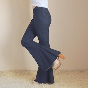 May include: Dark blue denim flare pants with a high waist. The pants are paired with a white top and a pair of beige and brown platform heels. The pants have a wide, flared leg opening.