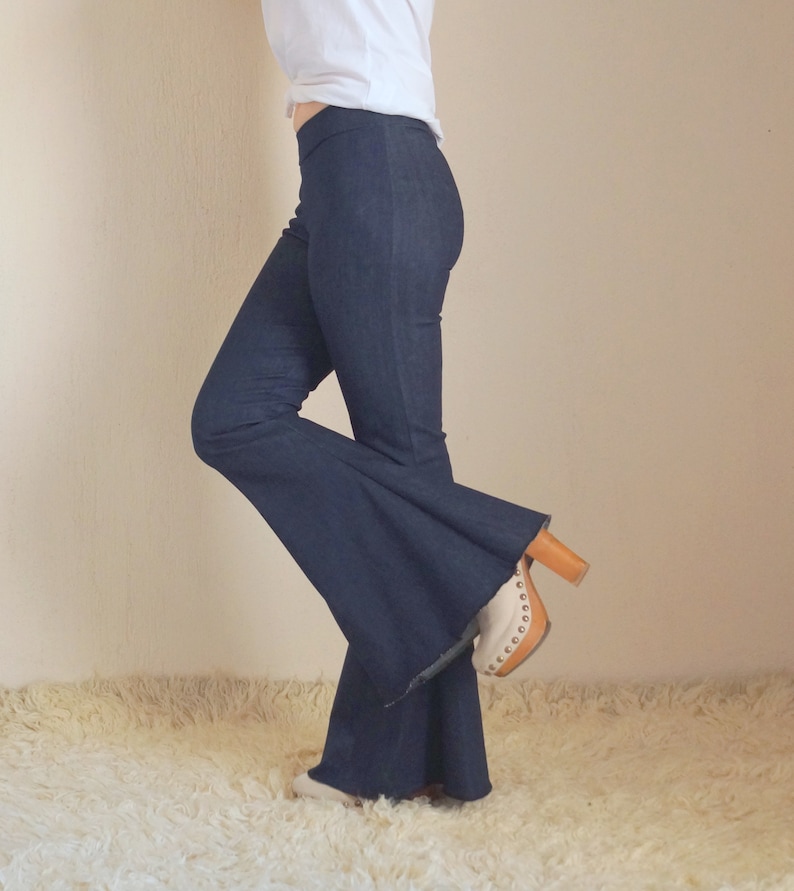 May include: Dark blue denim flare pants with a high waist. The pants are paired with a white top and a pair of beige and brown platform heels. The pants have a wide, flared leg opening.