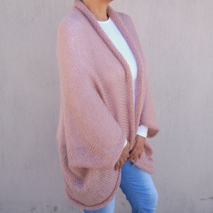 May include: A soft, blush pink knitted cardigan with a relaxed fit and long sleeves. The cardigan is open at the front and has a simple, elegant design.