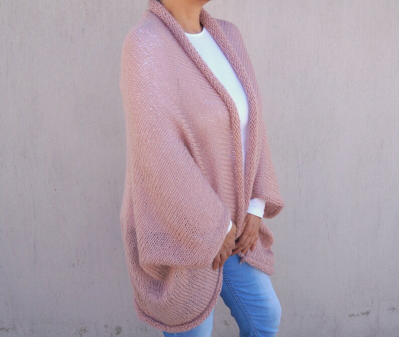 May include: A soft, blush pink knitted cardigan with a relaxed fit and long sleeves. The cardigan is open at the front and has a simple, elegant design.