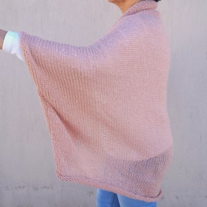 May include: A pale pink knitted poncho with a loose, flowing fit. The poncho is made of a soft, lightweight yarn and has a simple, elegant design.
