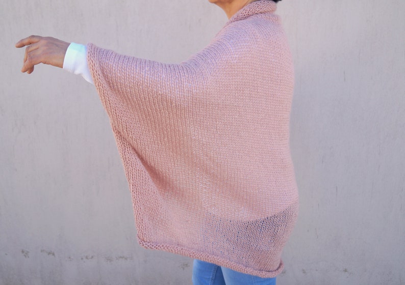 May include: A pale pink knitted poncho with a loose, flowing fit. The poncho is made of a soft, lightweight yarn and has a simple, elegant design.