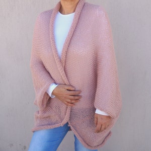 May include: A soft, blush pink knitted cardigan with a relaxed fit and long sleeves. The cardigan is open at the front and has a simple, elegant design.