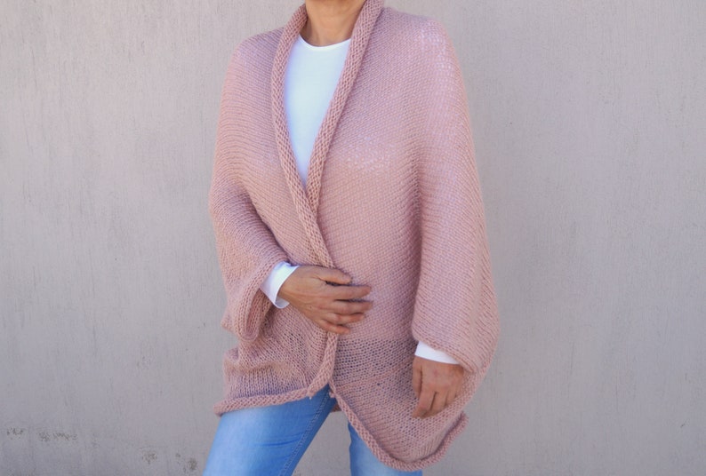 May include: A soft, blush pink knitted cardigan with a relaxed fit and long sleeves. The cardigan is open at the front and has a simple, elegant design.
