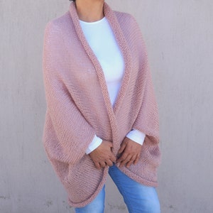 May include: A soft, blush pink knitted cardigan with a relaxed fit and long sleeves. The cardigan is open at the front and has a simple, elegant design.