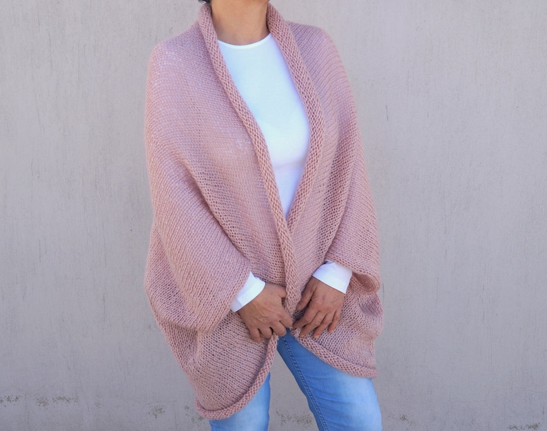 May include: A soft, blush pink knitted cardigan with a relaxed fit and long sleeves. The cardigan is open at the front and has a simple, elegant design.