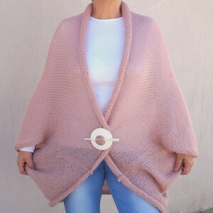 May include: A soft, pink knitted cardigan with a white button closure. The cardigan has a relaxed fit and a long, flowing silhouette.