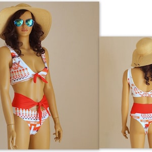 May include: A white and red patterned bikini with a high-waisted bottom and a knotted top. The bikini is tied at the waist and has a geometric pattern. The model is wearing a straw hat and sunglasses.