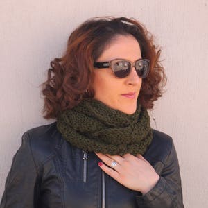 Könnte beinhalten: Eine Frau trägt einen dunkelgrünen, gestrickten Infinity-Schal und eine schwarze Lederjacke. Sie trägt eine Sonnenbrille und hat braunes Haar.