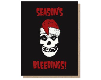 May include: Greeting card with a black background featuring a white skull wearing a red Santa hat. The text "SEASON'S BLEEDINGS!" is in red. The card has a brown border.