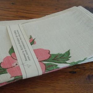 Pu&ograve; includere: Un set di tovaglioli di lino bianco con un motivo floreale rosa e verde. I tovaglioli sono orlati dalle Donne Cieche dell'Iowa, Commissione dello Stato dell'Iowa per i Ciechi.