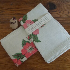 Pu&ograve; includere: Due asciugamani da t&egrave; in lino bianco con un motivo floreale di rose rosa e foglie verdi. Gli asciugamani sono piegati e hanno un'etichetta che recita "Hemmed by Blind Women of Iowa, Iowa State Commission for the Blind".