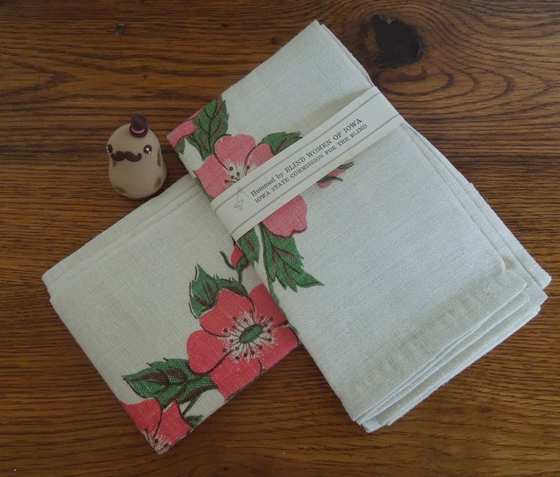 Pu&ograve; includere: Due asciugamani da t&egrave; in lino bianco con un motivo floreale di rose rosa e foglie verdi. Gli asciugamani sono piegati e hanno un'etichetta che recita "Hemmed by Blind Women of Iowa, Iowa State Commission for the Blind".