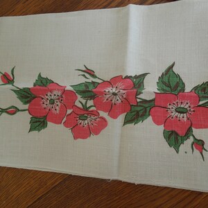 Pu&ograve; includere: Un asciugamano da cucina in lino bianco con un motivo floreale con rose rosa e foglie verdi.