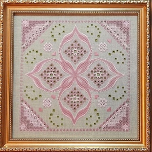 Op de afbeelding: Een ingelijst borduurwerk met een geometrisch ontwerp in roze en groene tinten. Het ontwerp heeft een centraal motief van vier overlappende vierkanten met ingewikkelde details. De achtergrond is een licht beige linnen stof.