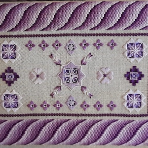 Op de afbeelding: Een paarse en witte borduurwerk sampler met verschillende steken en ontwerpen. De sampler is ingelijst met een paarse en witte rand.