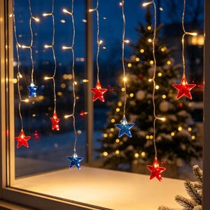 May include: A string of LED icicle lights hanging in a window, featuring alternating red and blue star-shaped ornaments. The clear wires are illuminated by warm white lights, creating a festive display against a dark evening backdrop.