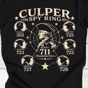May include: Black t-shirt featuring a graphic design related to the Culper Spy Ring. The design includes a portrait of George Washington, the text "CULPER SPY RING", and silhouettes of agents with numbers. A star and dot pattern surrounds the central image.