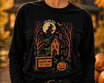 May include: Black long-sleeve shirt featuring a Halloween-themed graphic. The design includes a witch on a broom, a haunted house, a black cat, and a jack-o'-lantern. The text "Salem 400" and "Salem, MA EST. 1626" are also visible.