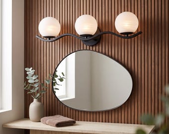 May include: A three-light vanity fixture featuring spherical frosted glass shades mounted on a black wavy metal bar, positioned above an asymmetrical, organic-shaped mirror with a thin black frame, creating a cohesive lighting arrangement.