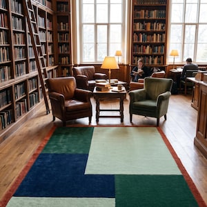 May include: A rectangular area rug featuring a geometric color-block pattern in shades of dark blue, forest green, and pale mint green, framed by a burnt orange border, laid out on a wooden floor in a library setting with armchairs.