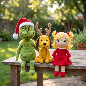 Puede incluir: Tres muñecos de ganchillo hechos a mano: una criatura verde con un gorro de Papá Noel rojo y blanco, un perro amarillo con astas marrones y una muñeca rubia con coletas que lleva un vestido rojo. Cada figura tiene detalles faciales cosidos.