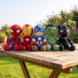 Op de afbeelding: Een set van vijf handgemaakte gehaakte poppen die superhelden voorstellen, waaronder Spider-Man in rood en blauw, Iron Man in rood en goud, Captain America in blauw, wit en rood, de Hulk in groen en paars, en Black Panther in het zwart.