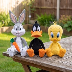 May include: Three handmade crochet dolls featuring a gray rabbit holding an orange carrot, a black duck with an orange beak, and a yellow bird with blue eyes. Each character is crafted with detailed yarn stitching and sits in an upright position.