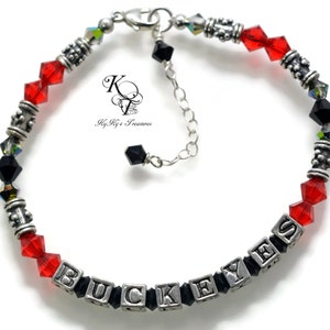 May include: A silver charm bracelet with red and black crystals and silver letter beads spelling "BUCK EYES".