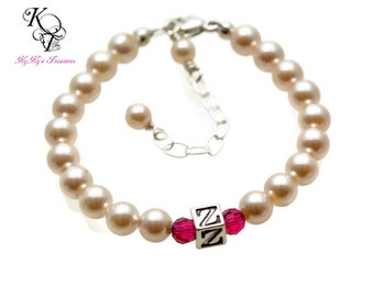 May include: A white pearl bracelet with a silver charm that says "Z" in block letters. The charm is surrounded by two pink crystals.