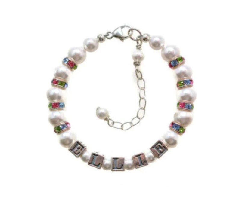 May include: A white pearl bracelet with a silver clasp and colorful crystal accents. The bracelet has a name spelled out in silver block letters: "ELLIE".
