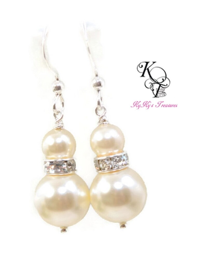 May include: A pair of silver dangle earrings with two ivory pearls and a row of clear rhinestones on each earring.