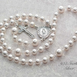 White pearl prayer beads on gray background. Pearls are spaced by silver lined clear seed beads. It has a sterling silver Virgin Mary Rosary Center charm and Sterling Silver Crucifix pendant.