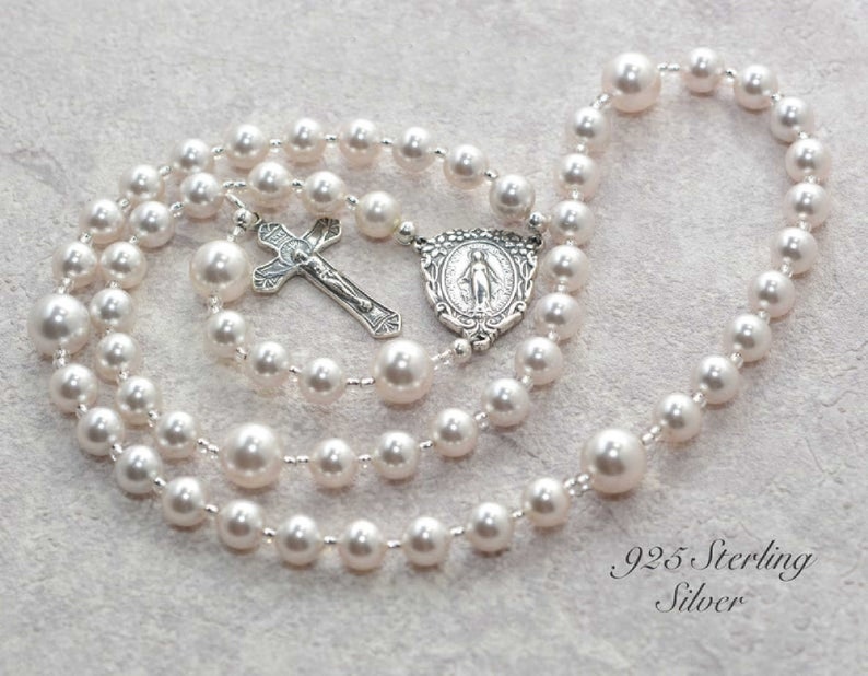 White pearl prayer beads on gray background. Pearls are spaced by silver lined clear seed beads. It has a sterling silver Virgin Mary Rosary Center charm and Sterling Silver Crucifix pendant.