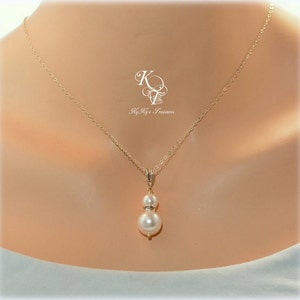 May include: A gold chain necklace with a double pearl pendant. The larger pearl is white and the smaller pearl is accented with small clear stones.